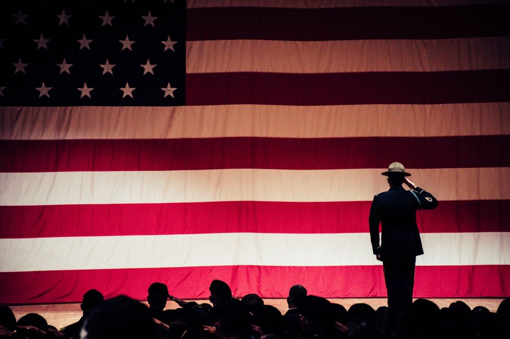 man standing on stage facing an american flag