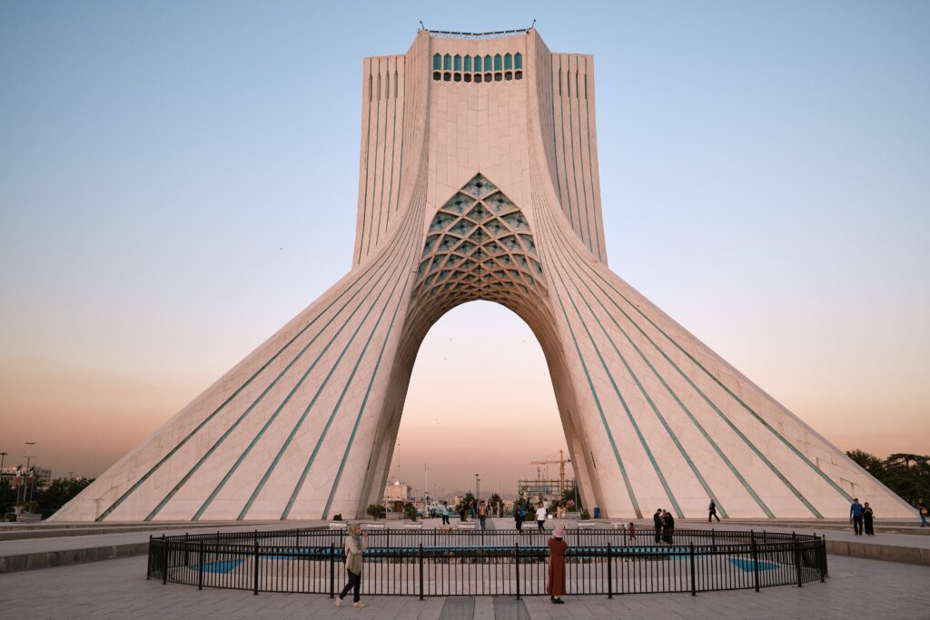 Azadi Tower in Tehran in warm evening light beneath a pale blue and pink sky.
