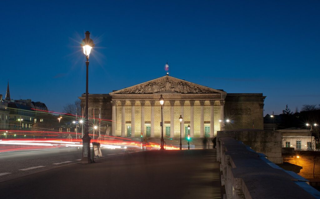 Palais Bourbon, home of the French National Assembly in Paris, illuminated at dusk; editorial illustration for France's debt and budget pressures.