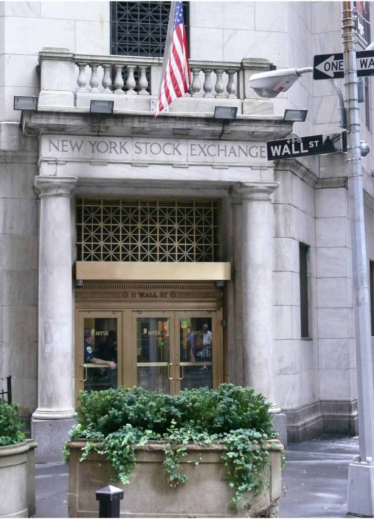 New York Stock Exchange entrance with an American flag and Wall Street sign.